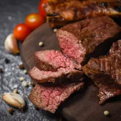 Soczyste steki wołowe na desce, z pomidorami i czosnkiem w tle. Unikaj najczęstsze błędy podczas przygotowywania steków wołowych na grillu, by osiągnąć taki efekt.
