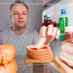 Mężczyzna sprawdza, ile czasu można bezpiecznie przechowywać ugotowane mięso w lodówce, widząc kiełbasy i kawałek boczku.