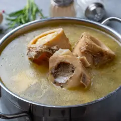 Gotuj najlepsze mięso na domowy bulion kolagenowy na stawy i gładką cerę. W garnku bulion z kości, obok marchew, cebula i zioła.