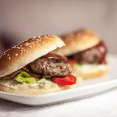 Dwa soczyste burgery wołowe na białym talerzu. Dowiedz się, jak smażyć burgery wołowe, żeby nie kurczyły się na patelni.