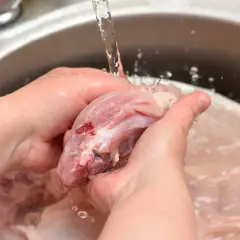 Ręce płuczą surowego kurczaka pod bieżącą wodą, co może zwiększyć wpływ mycia mięsa na rozprzestrzenianie bakterii w kuchni.