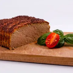Pokrojony pasztet na desce z pomidorkiem i bazylią.