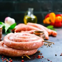 Surowe kiełbaski w jelitach, przyprawy, młynek do pieprzu i papryka na ciemnym tle.