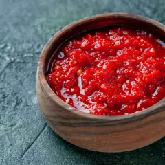 Afrykańska pasta, przyprawa harissa jak dawkować i do jakich potraw pasuje. Intensywnie czerwona, pikantna pasta w drewnianej miseczce.