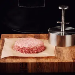 Surowy kotlet na desce i praska. Dowiedz się, dlaczego sól wyciąga wodę z mięsa i kiedy najlepiej solić steki.