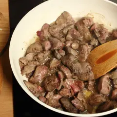 Smażona wątróbka w patelni z drewnianą łopatką, obok posiekana cebula.