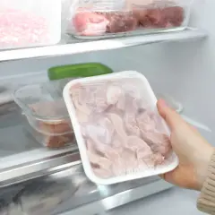 Ręka wyjmuje z lodówki opakowanie z zamrożonym mięsem. Dowiedz się, jak szybko rozmrozić mięso bez mikrofalówki, żeby nie namnożyć bakterii.