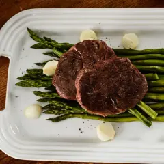 Dwa soczyste steki z polędwicy wołowej sous vide, podane z szparagami i czosnkiem. Idealny czas i temperatura gotowania dla perfekcyjnego smaku.