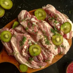 Surowe mięso wołowe z plasterkami kiwi i koperkiem, przygotowane do marynowania. Naturalna marynata do wołowiny z kiwi zmiękczająca mięso.