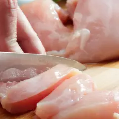 Dłoń kroi surowego kurczaka na desce. Czy zjedzenie niedosmażonego kurczaka zawsze kończy się zatruciem pokarmowym? Niekoniecznie, ale ryzyko jest wysokie.