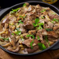 Wątróbka wołowa z pieczarkami w sosie, udekorowana natką pietruszki, podana na patelni.
