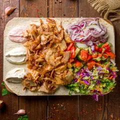 Kebab z baraniny na placku z warzywami, sosami i przyprawami na drewnianym tle.