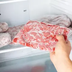 Ręka wyjmuje z zamrażarki paczkę mrożonej surowej karkówki. Dowiedz się, jak długo można mrozić surową karkówkę, żeby nie zjełczał w niej tłuszcz.