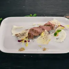 Pokrojona cielęcina z kremowym sosem, chrupiącymi dodatkami i ziołami na białym talerzu.