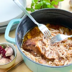 Szarpana wieprzowina w sosie, rozrywana widelcami w naczyniu żeliwnym, obok czosnek i papryczka chili.