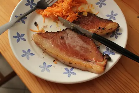 Smażona wieprzowina z marketu puszcza soki, bo zawiera dużo wody. Na talerzu z surówką z marchewki widać dwa kawałki mięsa.