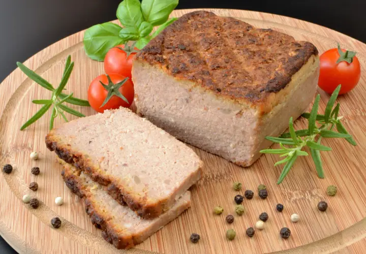 Upieczony pasztet na desce z pomidorkami, rozmarynem i pieprzem.
