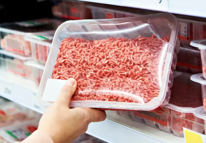 Ręka wybiera mięso mielone z supermarketu, skłaniając do analizy ukrytych konserwantów i soli.