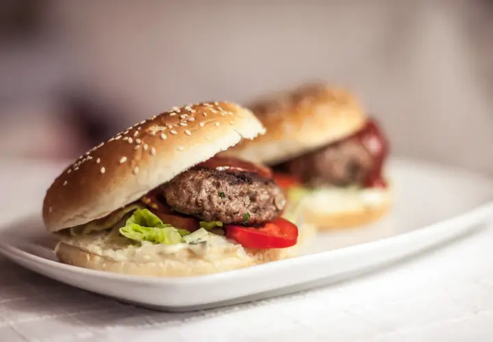 Dwa soczyste burgery wołowe na białym talerzu. Dowiedz się, jak smażyć burgery wołowe, żeby nie kurczyły się na patelni.