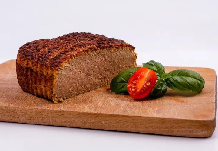 Pokrojony pasztet na desce z pomidorkiem i bazylią.
