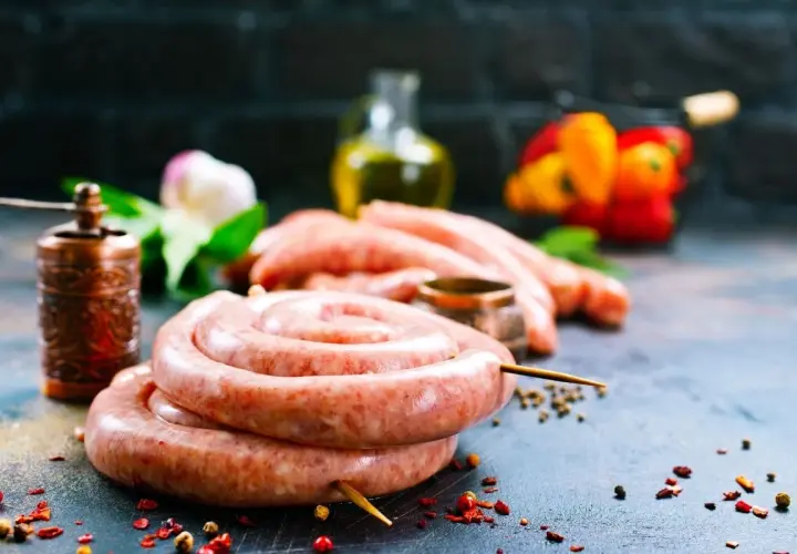 Surowe kiełbaski w jelitach, przyprawy, młynek do pieprzu i papryka na ciemnym tle.