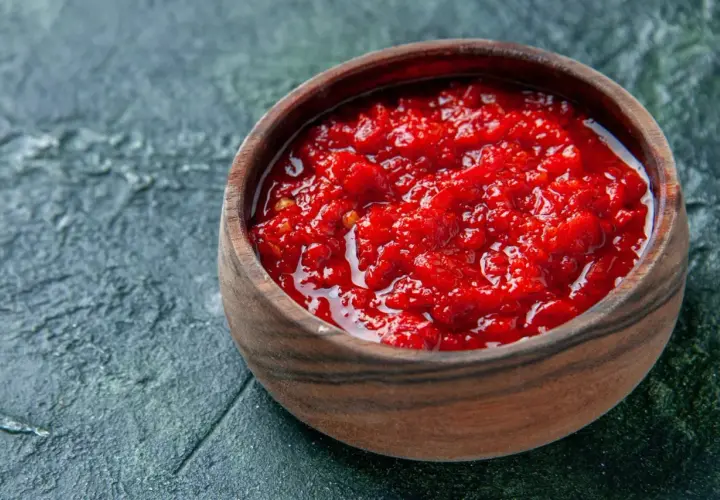 Afrykańska pasta, przyprawa harissa jak dawkować i do jakich potraw pasuje. Intensywnie czerwona, pikantna pasta w drewnianej miseczce.