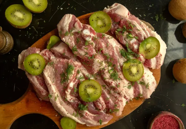 Surowe mięso wołowe z plasterkami kiwi i koperkiem, przygotowane do marynowania. Naturalna marynata do wołowiny z kiwi zmiękczająca mięso.