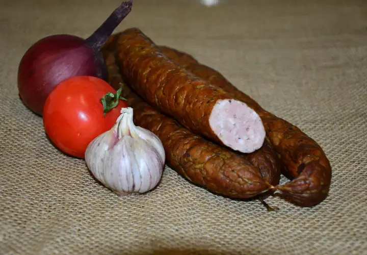 Kiełbasa, cebula, pomidor i czosnek na płóciennym tle.