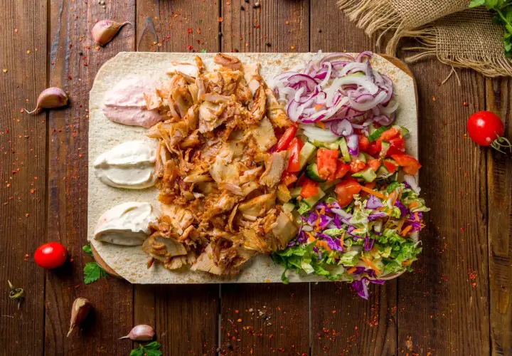 Kebab z baraniny na placku z warzywami, sosami i przyprawami na drewnianym tle.