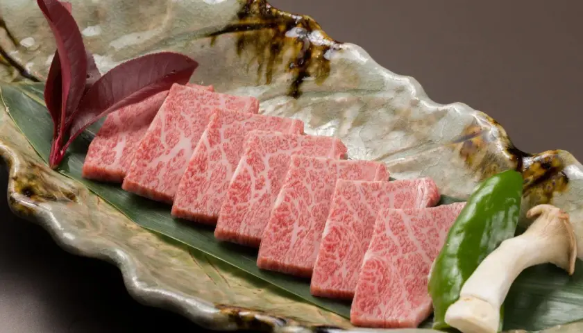 Wołowina wagyu a kobe: czym dokładnie różnią się te gatunki? Delikatne plastry marmurkowego mięsa na liściu, z pieprzem i grzybami.