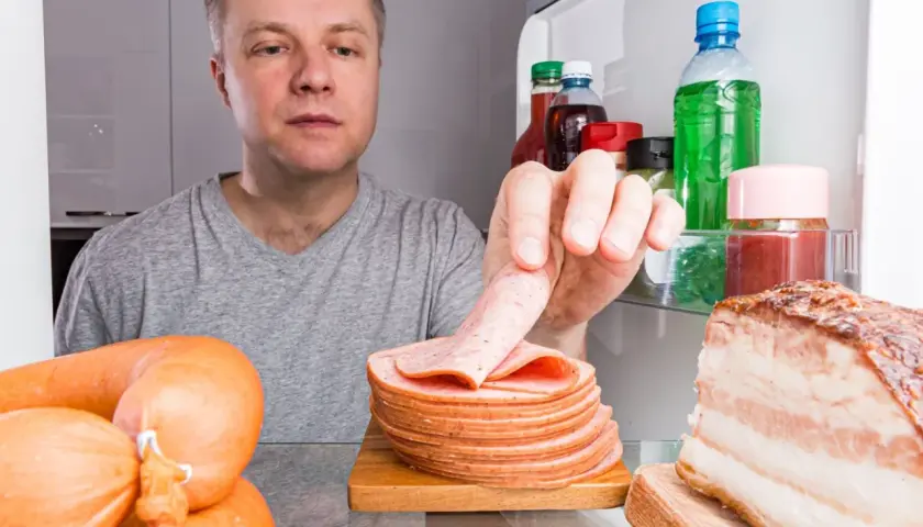 Mężczyzna sprawdza, ile czasu można bezpiecznie przechowywać ugotowane mięso w lodówce, widząc kiełbasy i kawałek boczku.