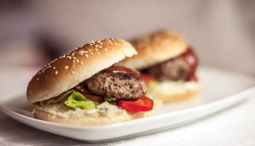 Dwa soczyste burgery wołowe na białym talerzu. Dowiedz się, jak smażyć burgery wołowe, żeby nie kurczyły się na patelni.