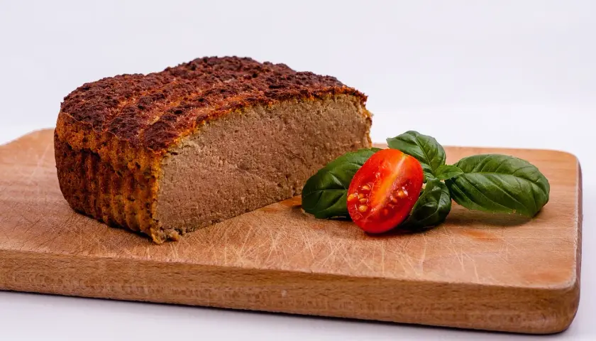 Pokrojony pasztet na desce z pomidorkiem i bazylią.