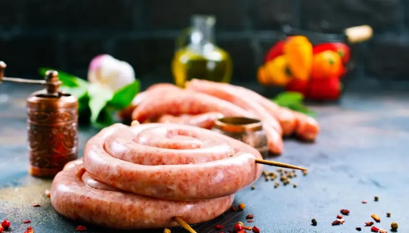 Surowe kiełbaski w jelitach, przyprawy, młynek do pieprzu i papryka na ciemnym tle.