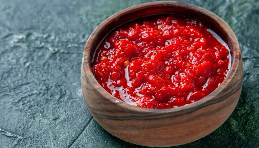 Afrykańska pasta, przyprawa harissa jak dawkować i do jakich potraw pasuje. Intensywnie czerwona, pikantna pasta w drewnianej miseczce.