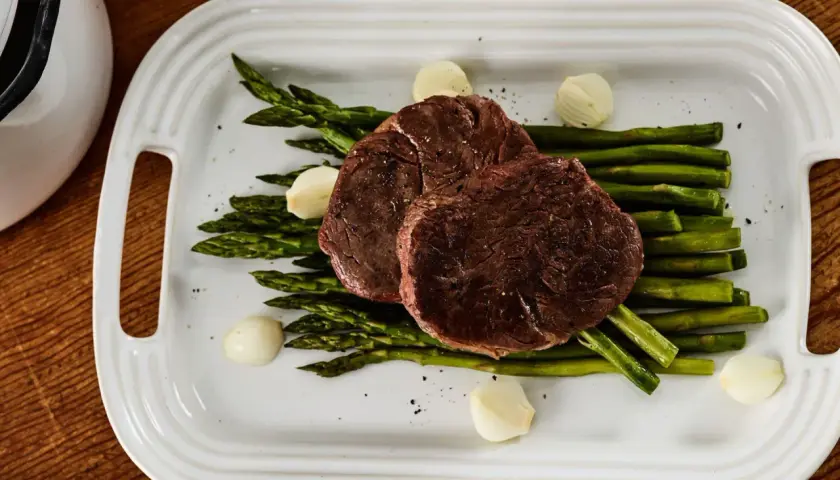 Dwa soczyste steki z polędwicy wołowej sous vide, podane z szparagami i czosnkiem. Idealny czas i temperatura gotowania dla perfekcyjnego smaku.