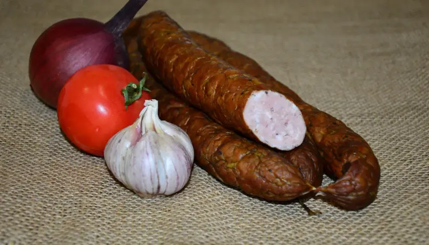 Kiełbasa, cebula, pomidor i czosnek na płóciennym tle.
