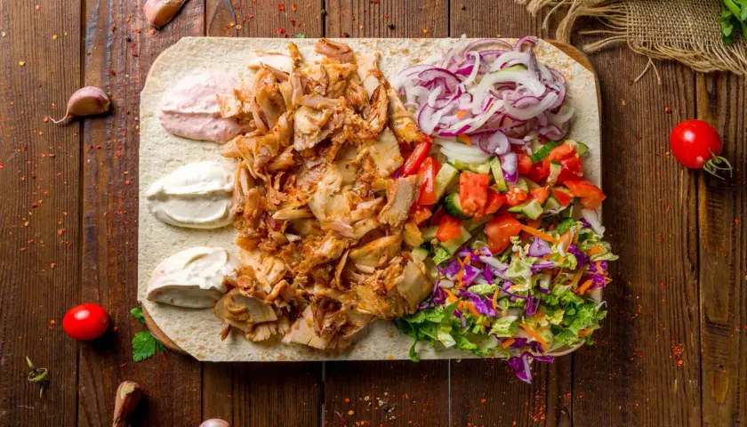 Kebab z baraniny na placku z warzywami, sosami i przyprawami na drewnianym tle.