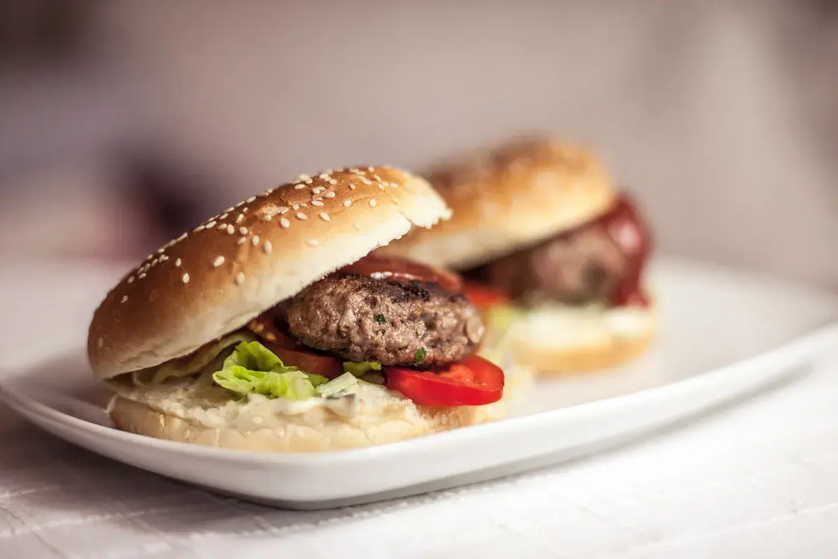 Dwa soczyste burgery wołowe na białym talerzu. Dowiedz się, jak smażyć burgery wołowe, żeby nie kurczyły się na patelni.