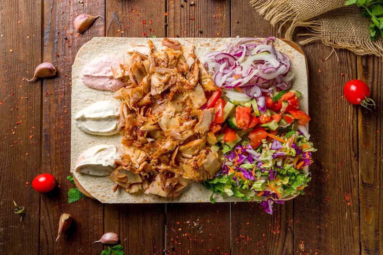 Kebab z baraniny na placku z warzywami, sosami i przyprawami na drewnianym tle.