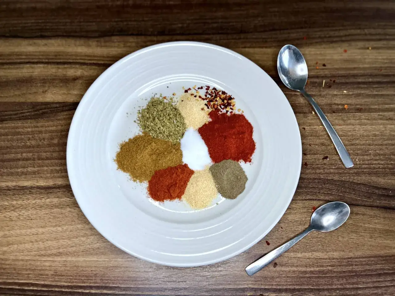 Jak przygotować przyprawę taco we własnym domu lepszą niż gotowa z torebki? Na talerzu kolorowe przyprawy: papryka, kmin, oregano, czosnek, sól, chili.