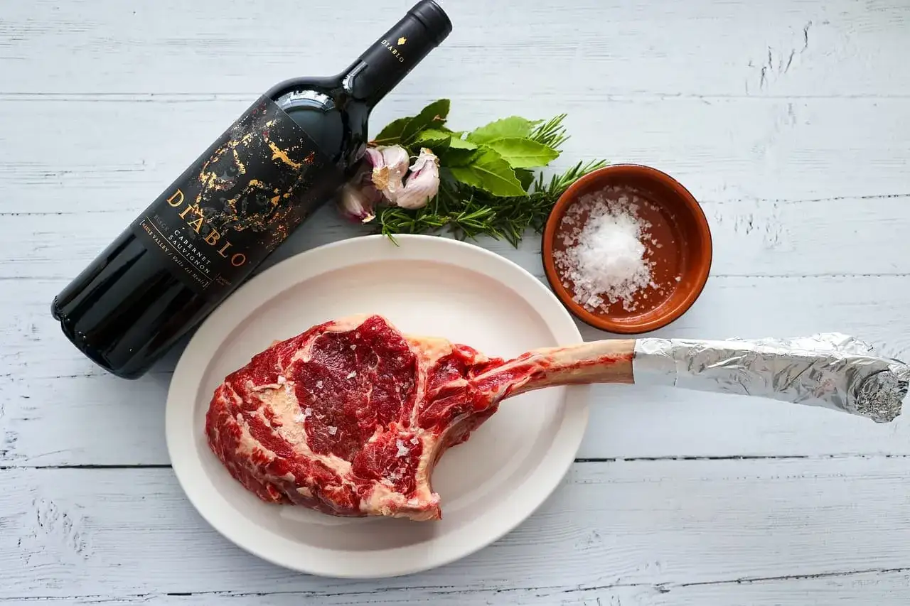 Wina czerwone do wołowiny: jak dobrać odpowiedni szczep? Na stole surowy stek, butelka wina Diablo Cabernet Sauvignon, czosnek, zioła i sól.