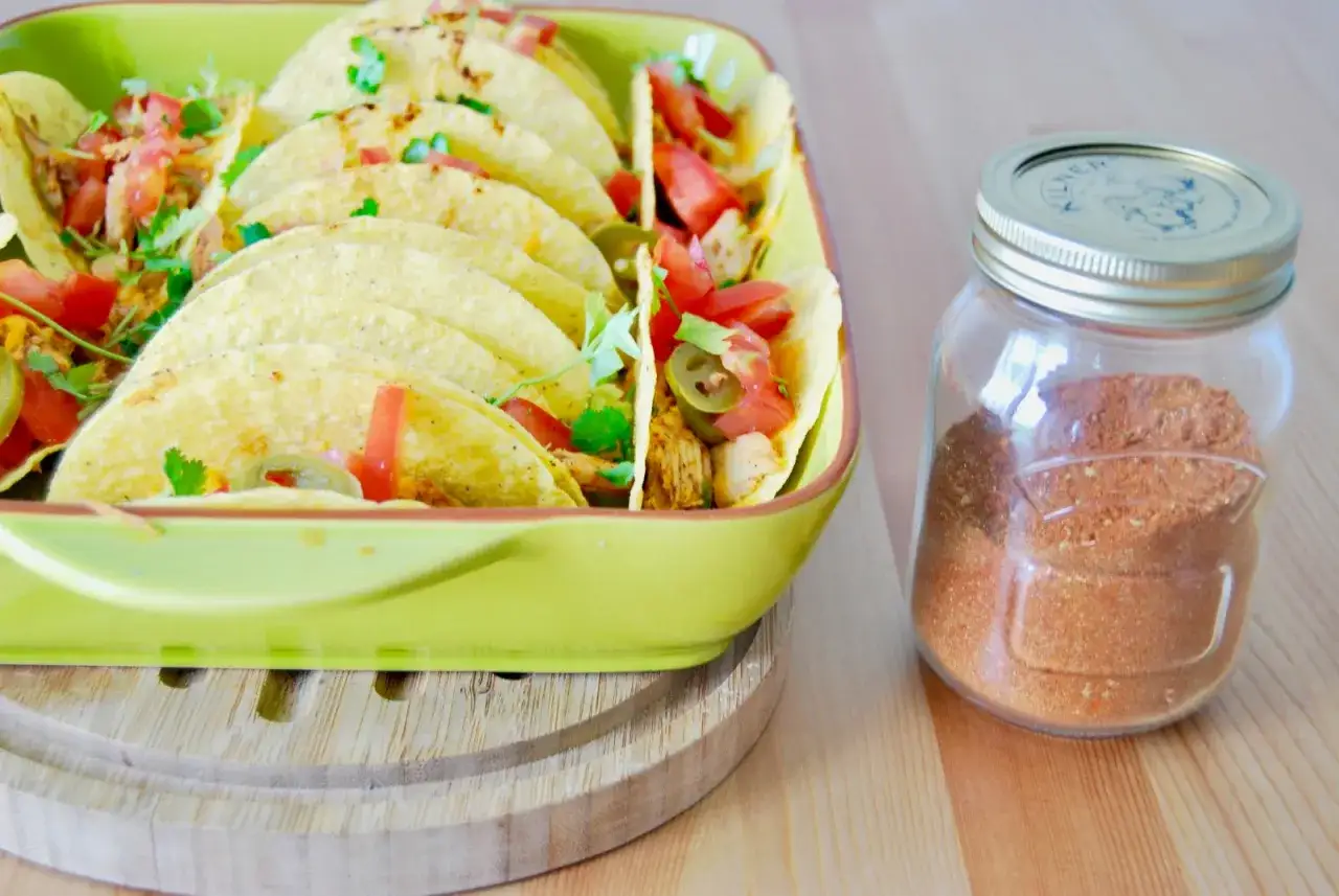 Domowa przyprawa do taco w słoiku obok talerza z gotowymi taco. Dowiedz się, jak przygotować przyprawę taco we własnym domu lepszą niż gotowa z torebki.