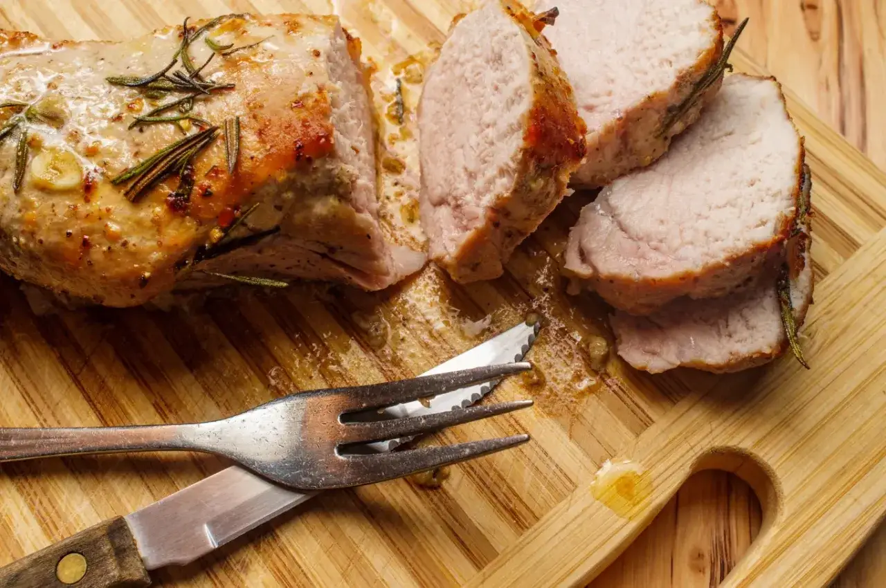 Pieczony schab z rozmarynem, pokrojony w plastry. Czy jedzenie niedopieczonej wieprzowiny grozi zakażeniem włośnicą? Uważaj na surowe mięso.