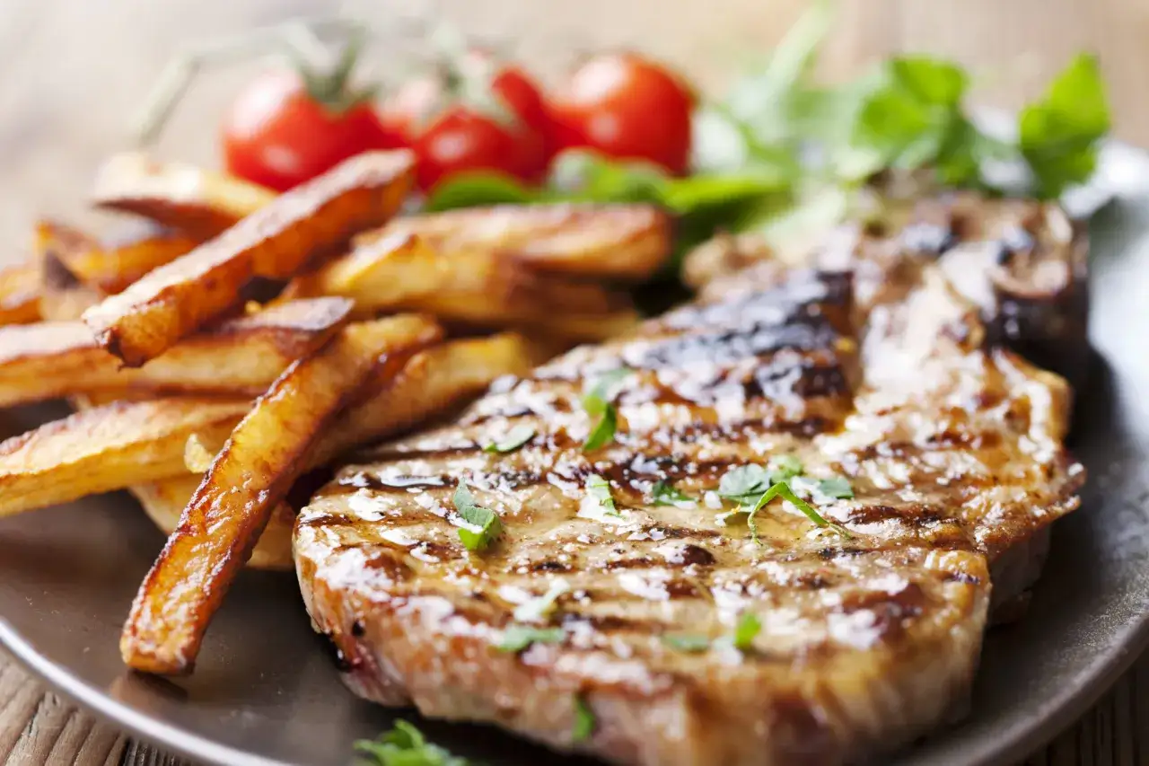 Grillowany stek z frytkami i pomidorkami. Sól wyciąga wodę z mięsa, dlatego najlepiej solić steki tuż przed smażeniem.