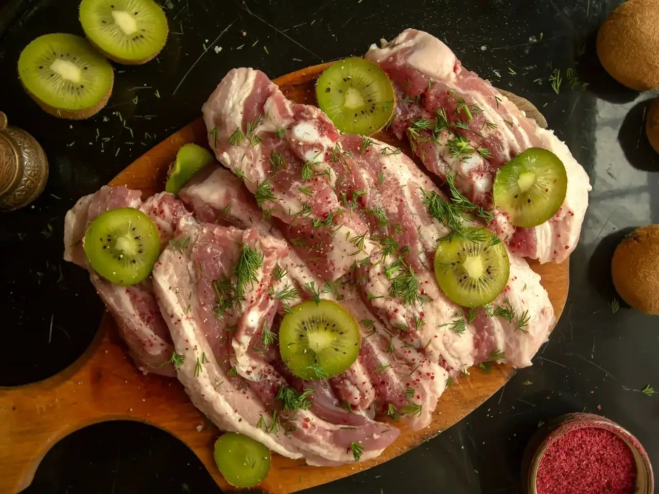 Surowe mięso wołowe z plasterkami kiwi i koprem, przygotowane do marynowania. Naturalna marynata do wołowiny z kiwi zmiękczająca mięso.