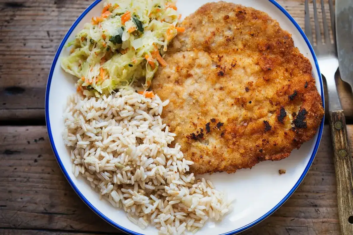 Smażony kotlet drobiowy z ryżem i surówką. Chcesz wiedzieć, jak odgrzać smażonego kotleta drobiowego, żeby panierka znowu była chrupiąca?